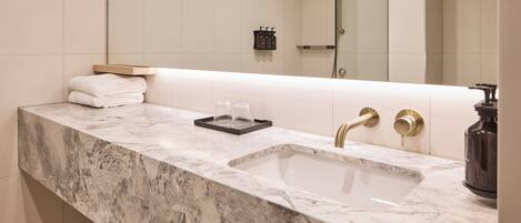 A bathroom with a marble sink, two gold faucets, a glass soap dish, and a towel rack.