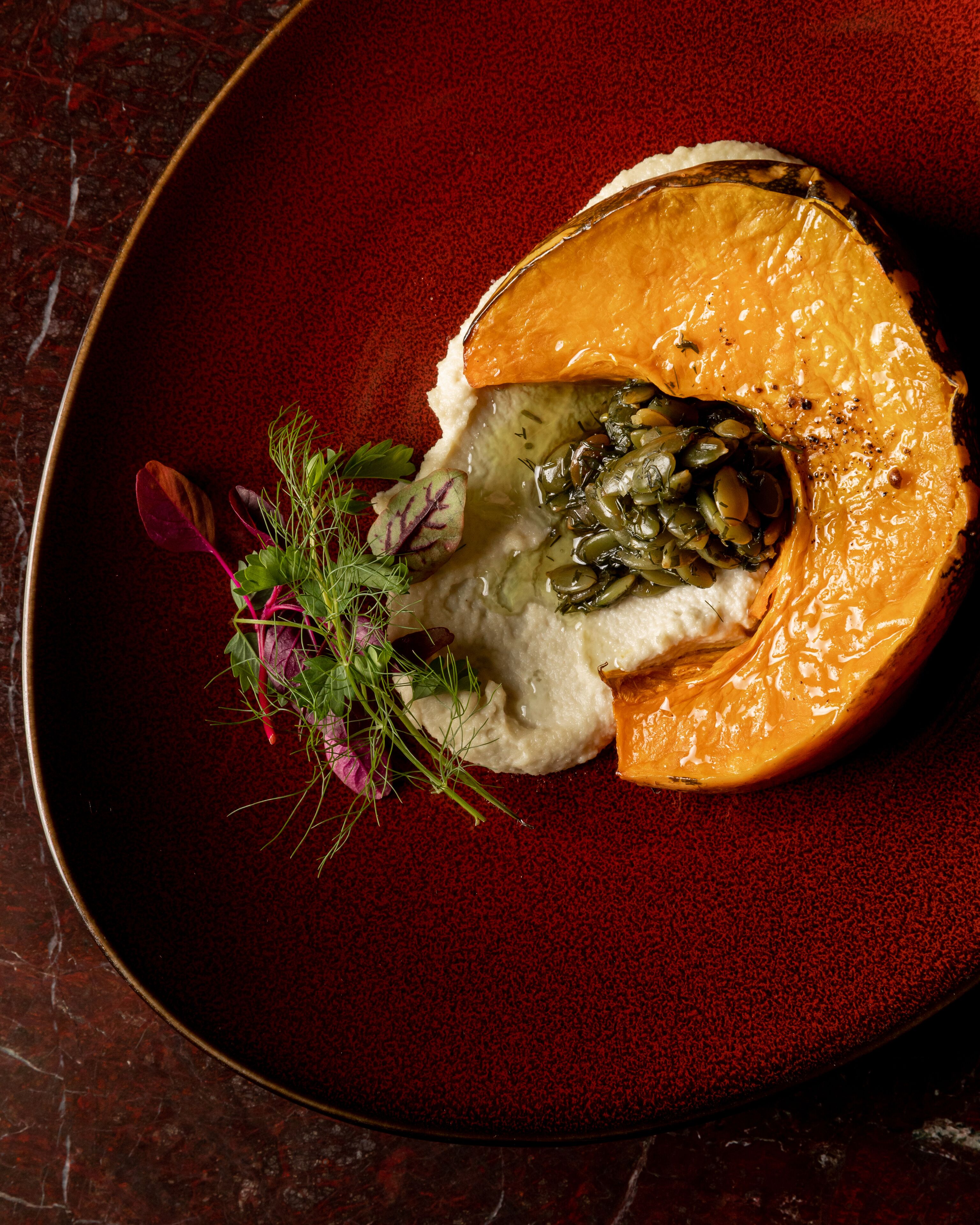 A dish with a roasted vegetable and greens on a dark plate.
