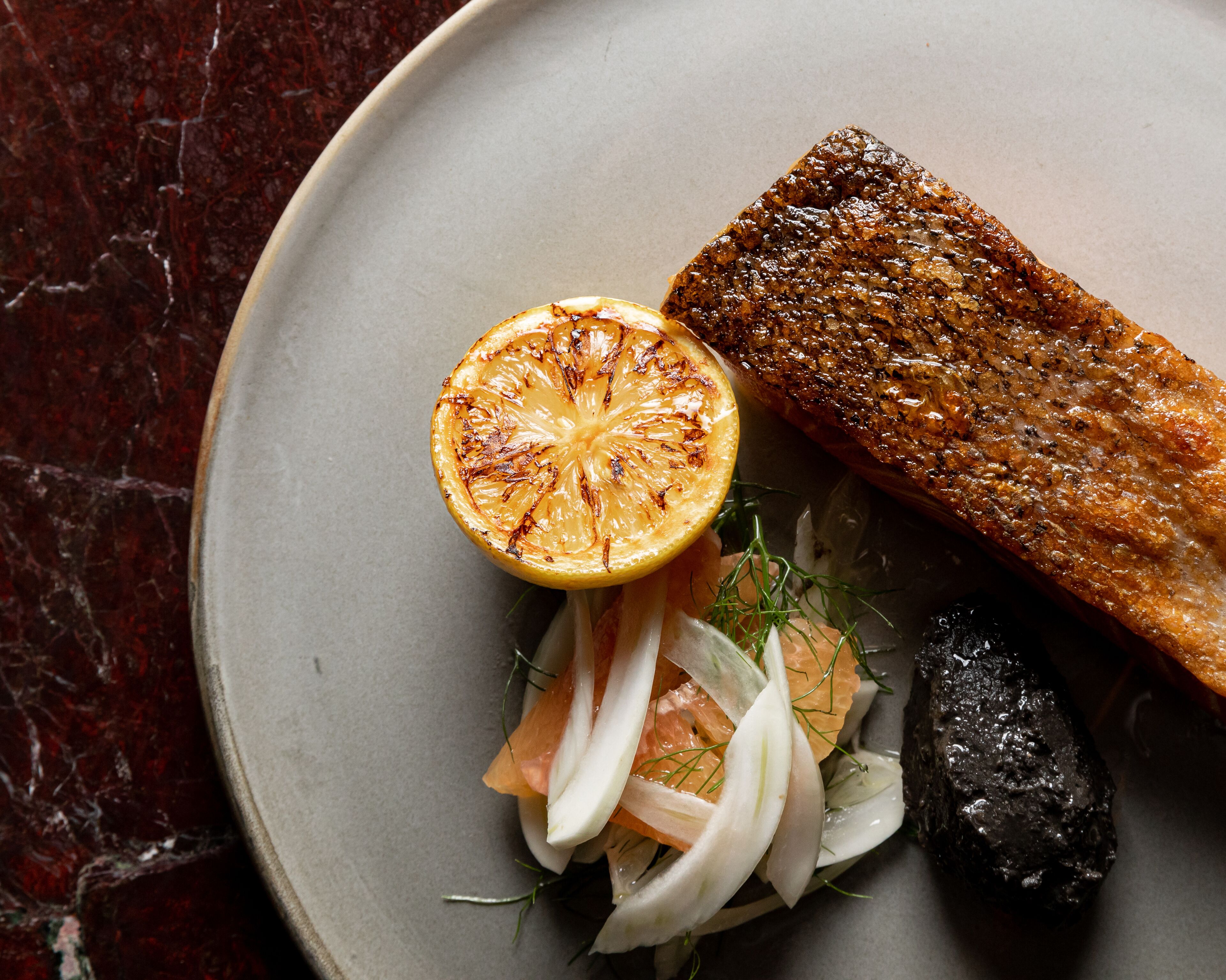 A plate with a grilled fish, a slice of grilled lemon, and a side salad.
