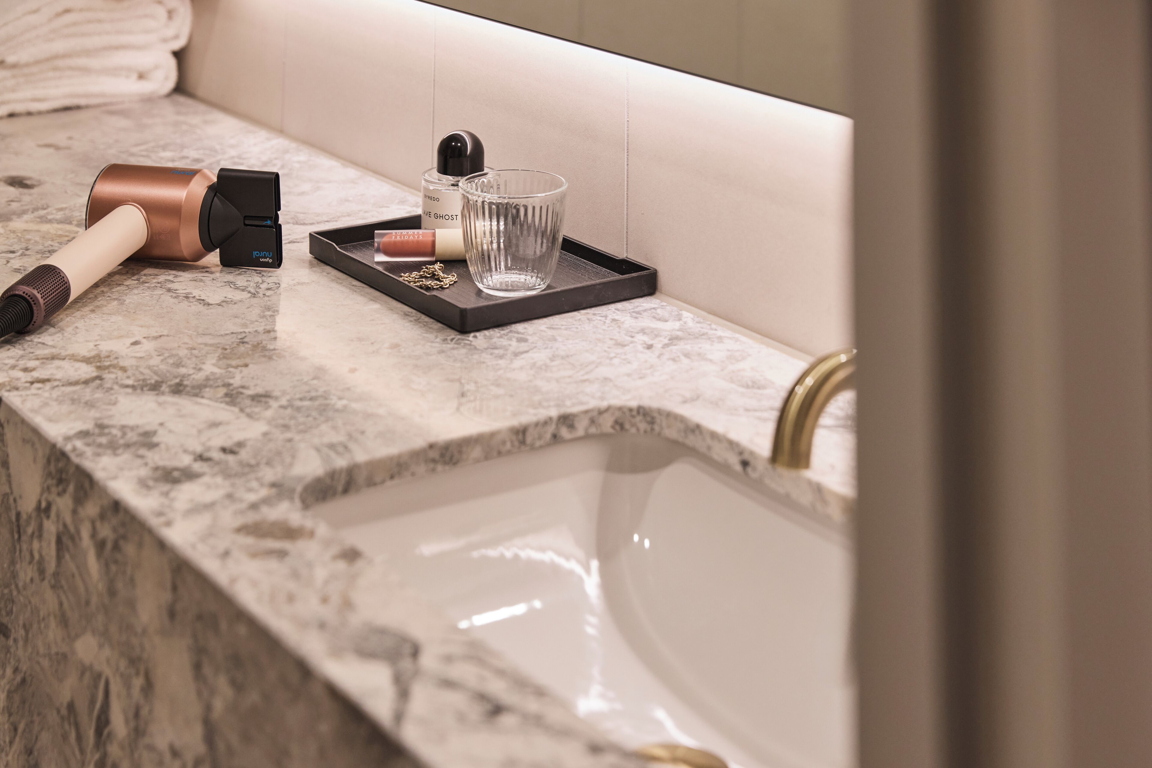 A bathroom with a marble countertop, a handheld vacuum cleaner, a glass, and a tray with toiletries.