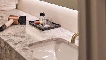 A bathroom with a marble countertop, a handheld vacuum cleaner, a glass, and a tray with toiletries.
