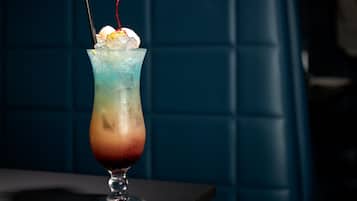 Um cocktail num copo alto com efeito degradê de cores, cubos de gelo e uma cereja por cima.