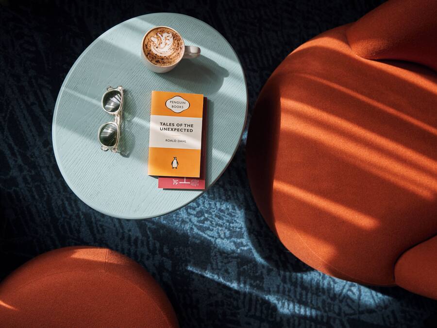 A round table with a book, a pair of sunglasses, and a cup of coffee.