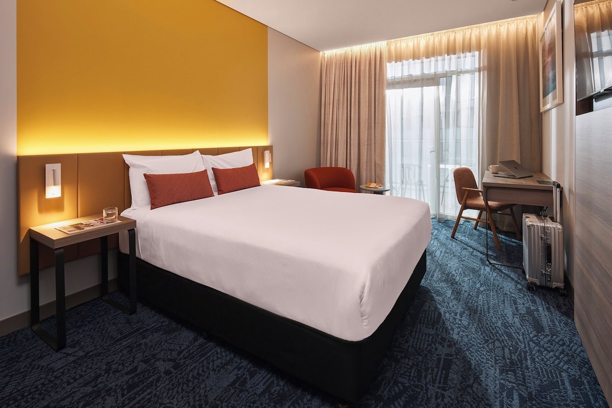 A hotel room with a large bed, a desk with a laptop, and a suitcase.