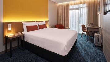 Una habitación de hotel con una cama grande, un escritorio con una computadora portátil y una maleta.