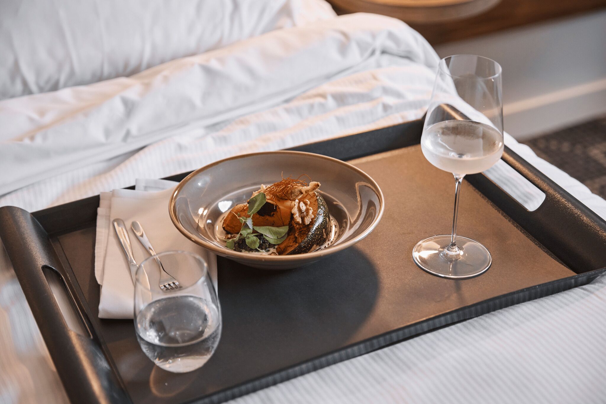 Uma bandeja com uma tigela de comida, uma taça de vinho e talheres sobre a cama.