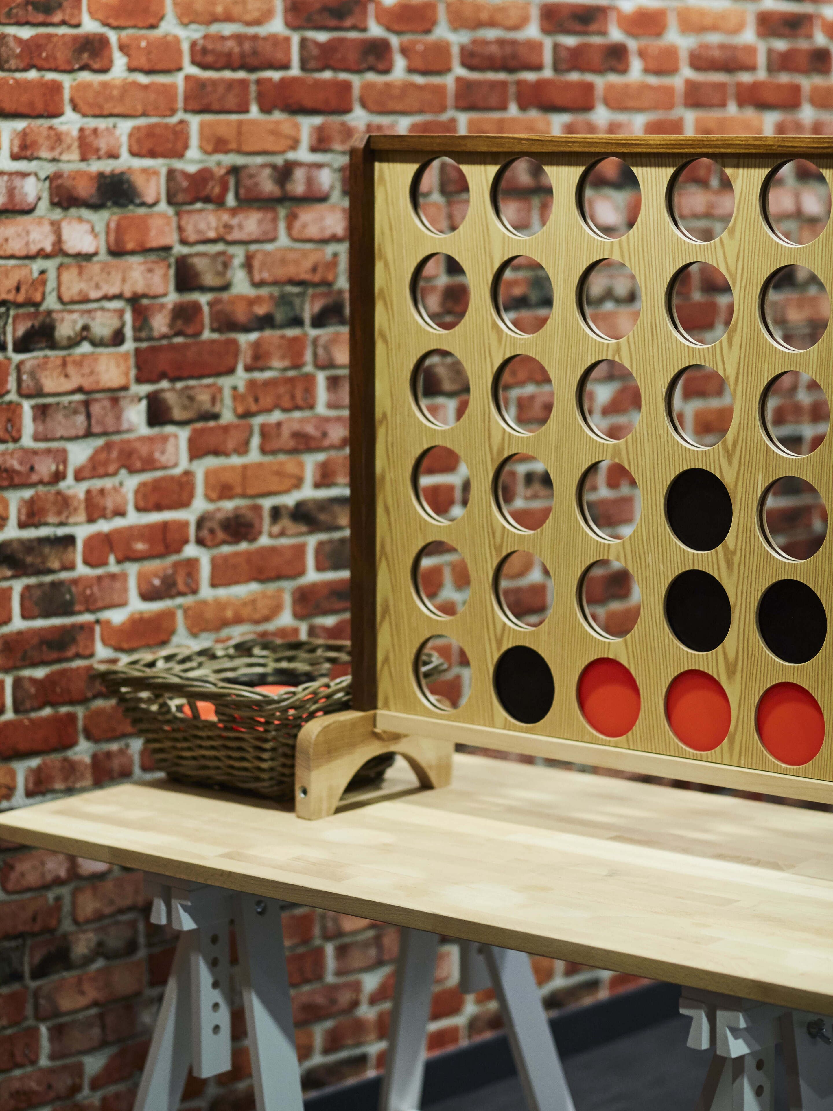 A wooden board with circular cutouts, a basket, and a metal stand on a table against a brick wall.