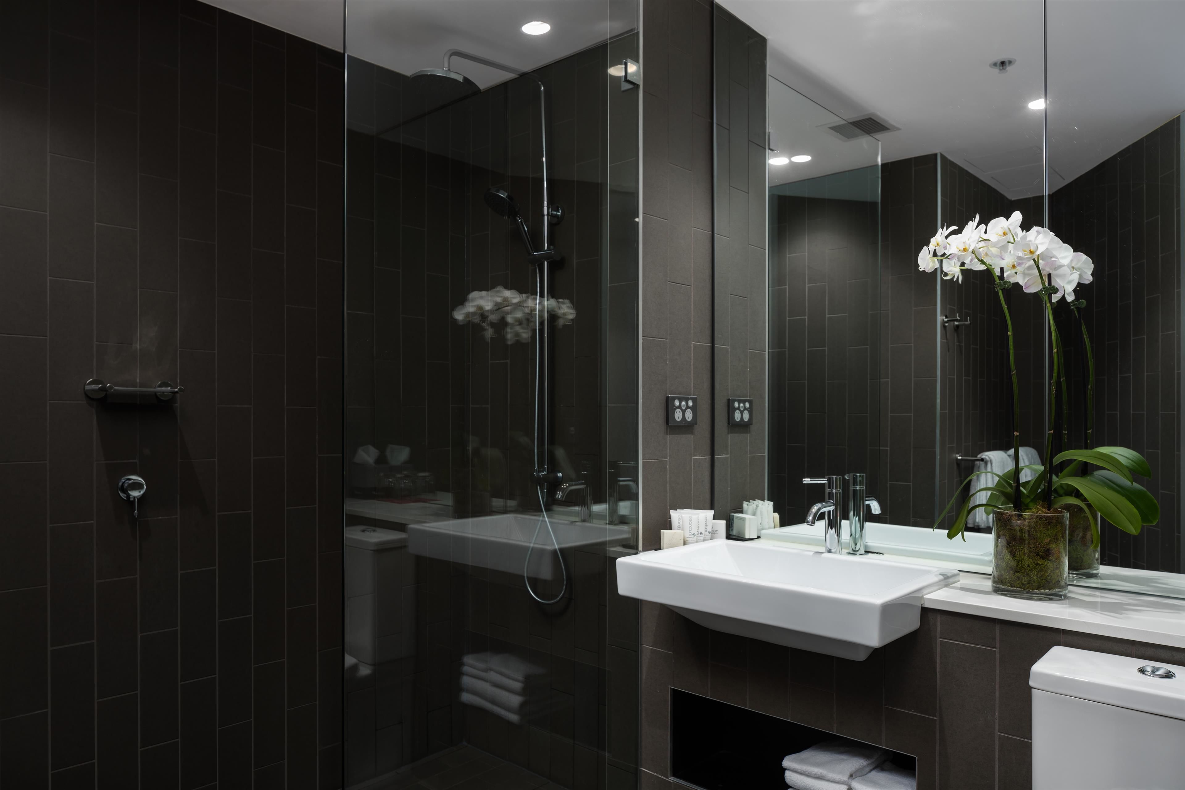 A modern bathroom with a glass-enclosed shower, a white sink, and a large mirror.