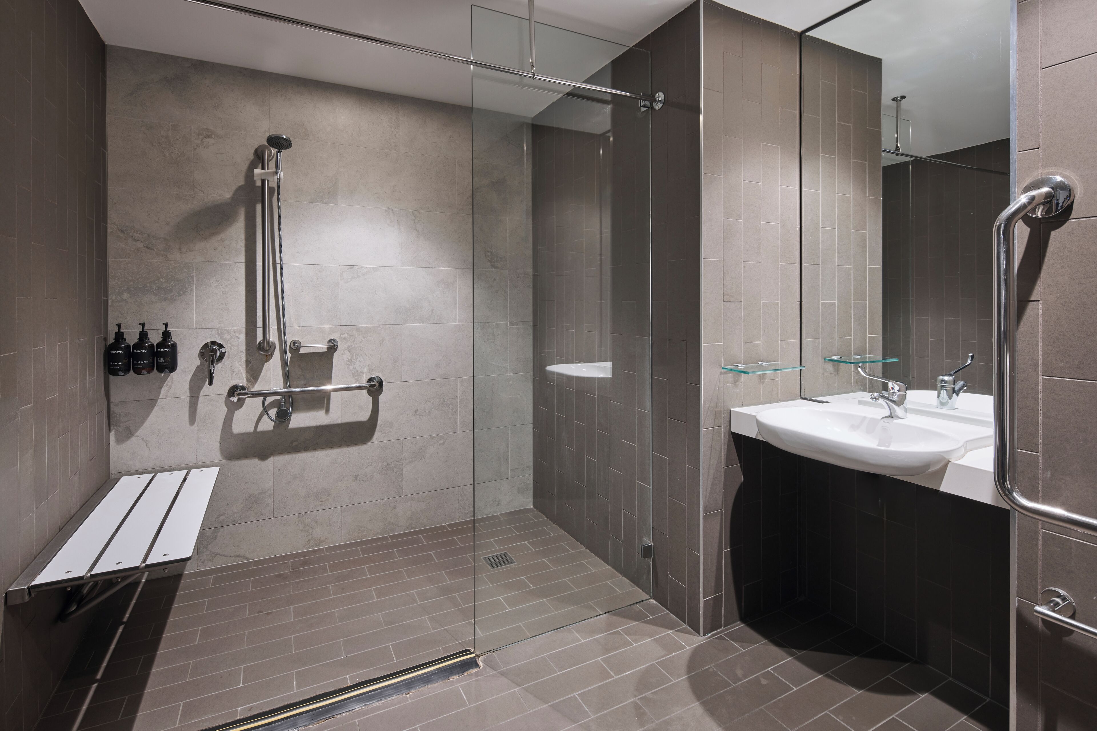 A modern bathroom with a glass-enclosed shower, a white sink, and a glass shelf.