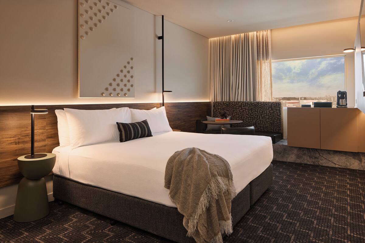 A modern hotel room with a large bed, a bedside table, a coffee machine, and a view of the city through the window.