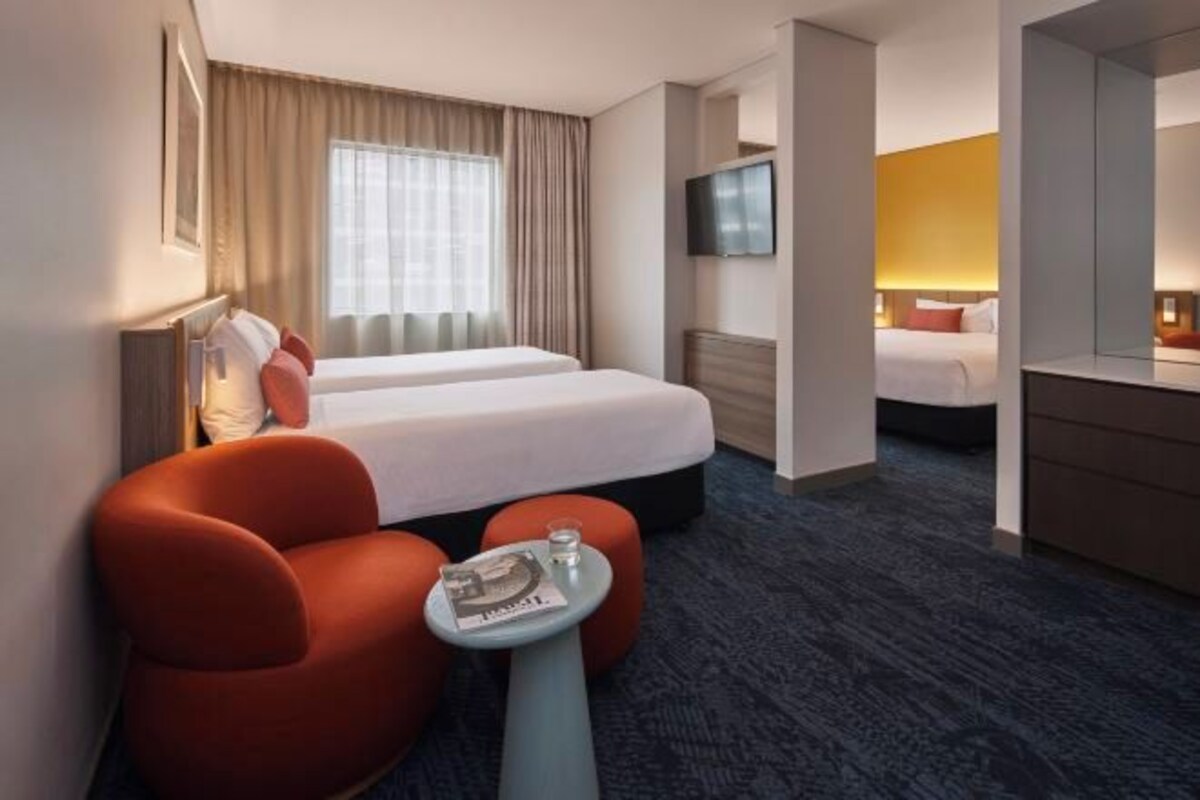 A hotel room with two beds, a TV, a small table with a magazine, and a red armchair.