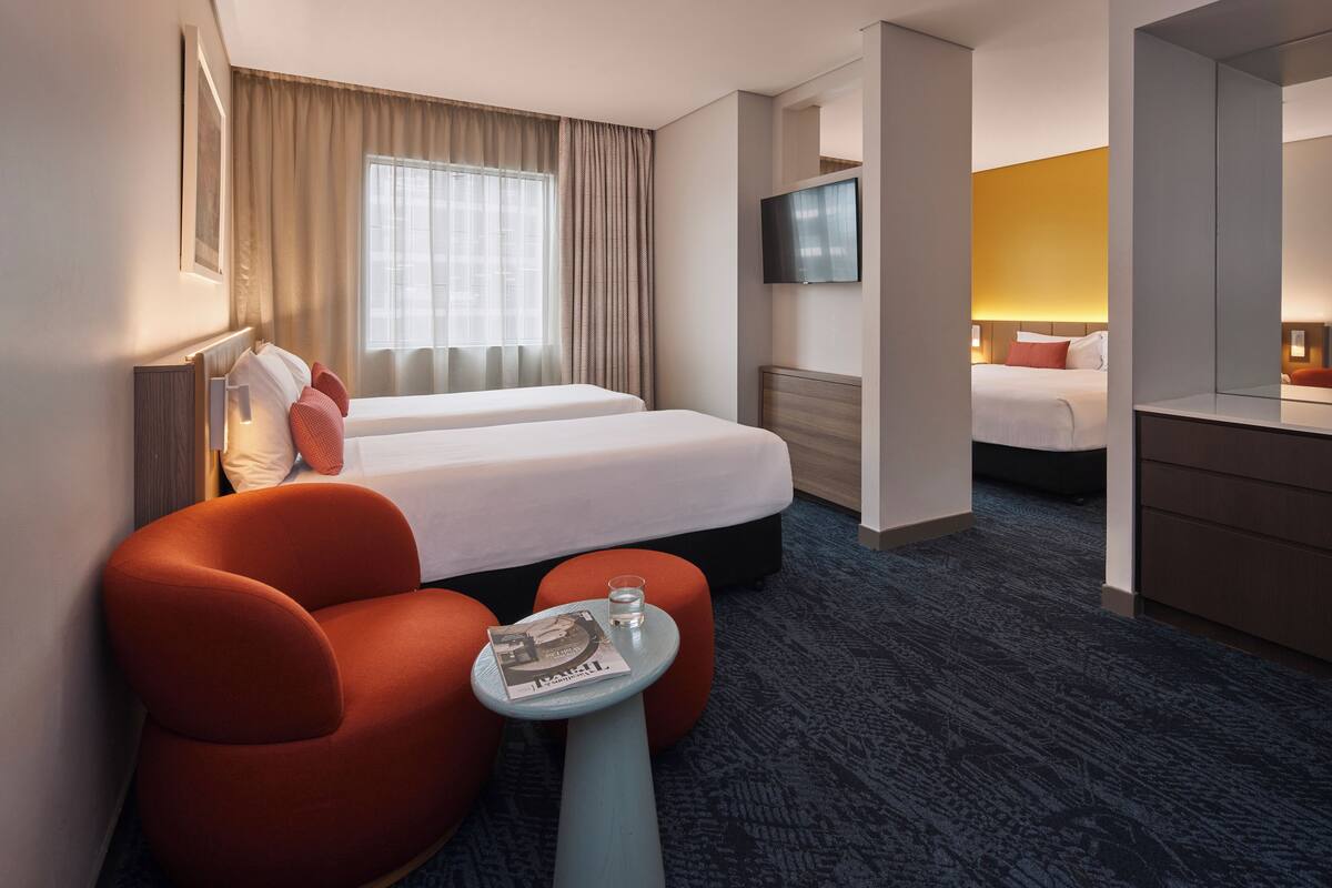 A hotel room with two beds, a TV, a small table with a magazine, and a large mirror.