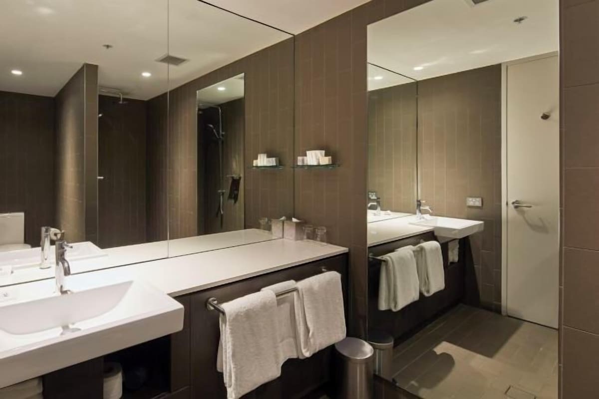 A modern bathroom with two sinks, a large mirror, and a shower area.
