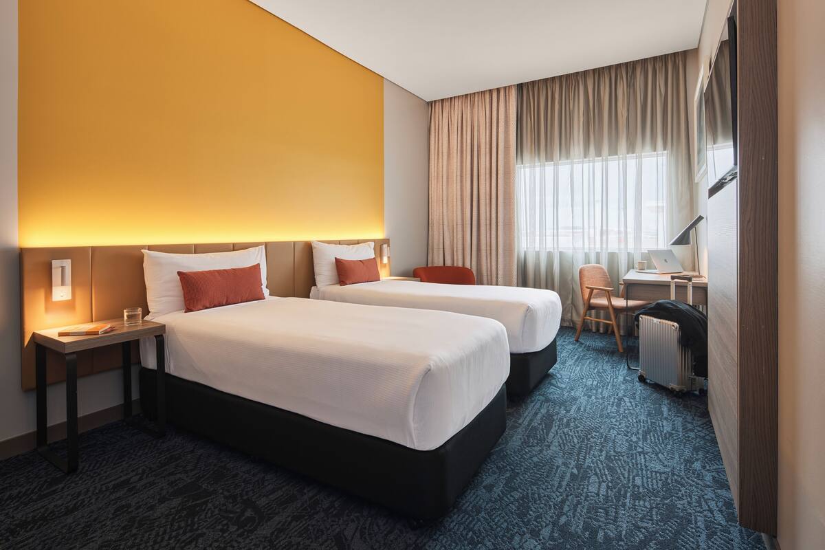 A hotel room with two beds, a desk, a chair, and a radiator.