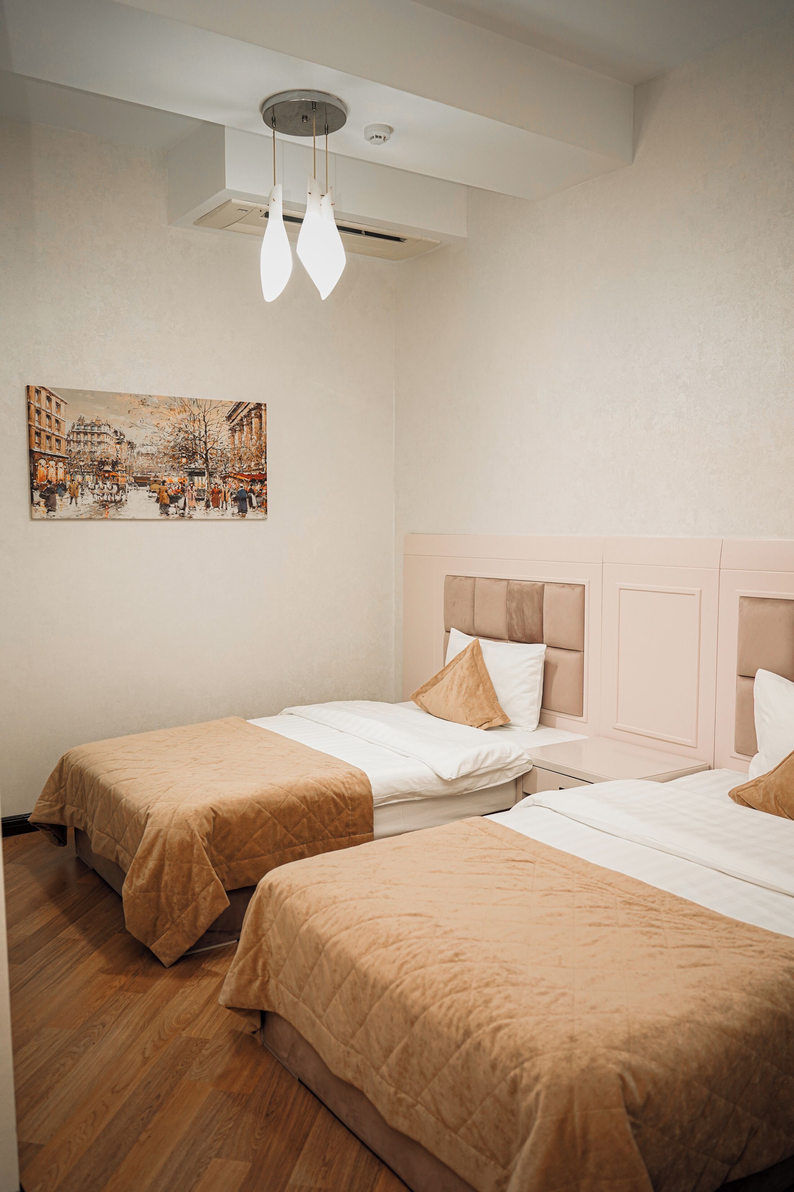 Ein Hotelzimmer mit zwei Betten, einer Deckenleuchte und einem an der Wand hängenden Gemälde.