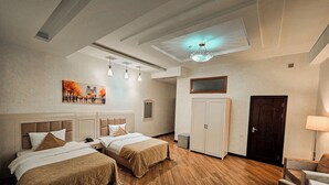 A hotel room with two beds, wooden flooring, a ceiling light, a painting, a wardrobe, and a door. - Safran Hotel (Baku)