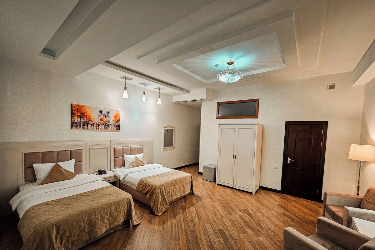 A hotel room with two beds, wooden flooring, a ceiling light, a painting, a wardrobe, and a door.