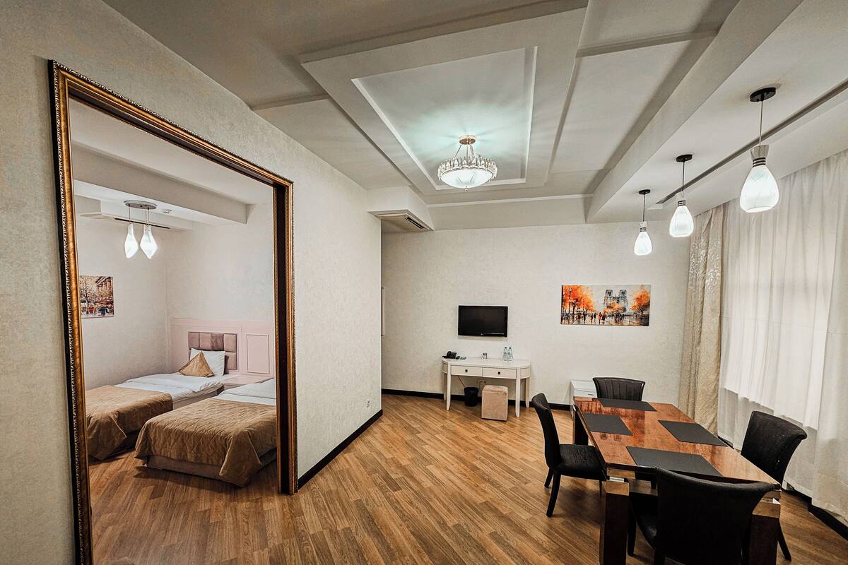 A hotel room with a wooden floor, a dining area with a table and chairs, a TV, and a large mirror.