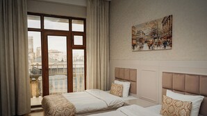 A hotel room with two beds, a large window with curtains, and a cityscape painting on the wall. - Safran Hotel (Baku)