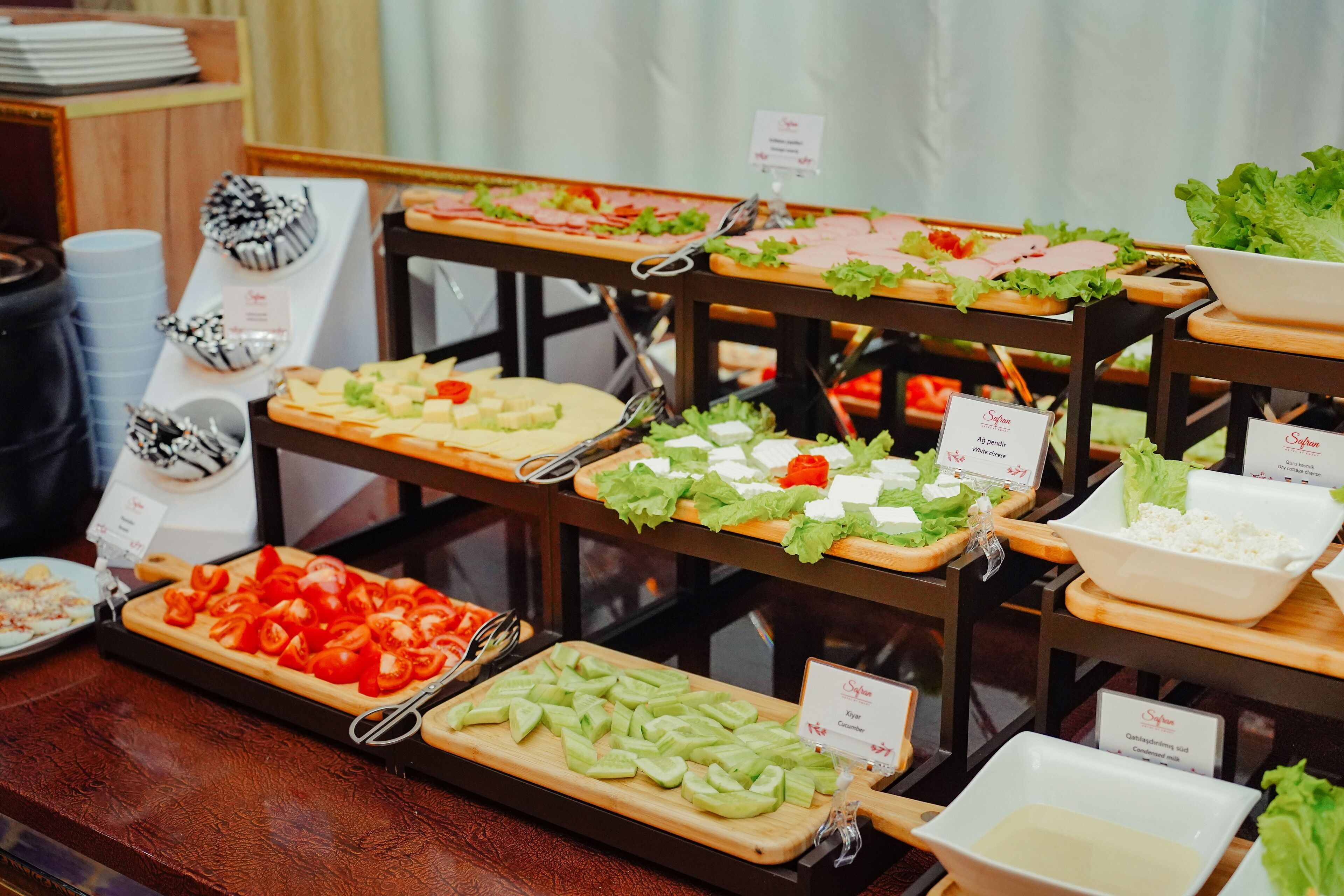 A buffet with various food items including sliced tomatoes, cucumbers, and leafy greens, arranged on wooden serving boards.