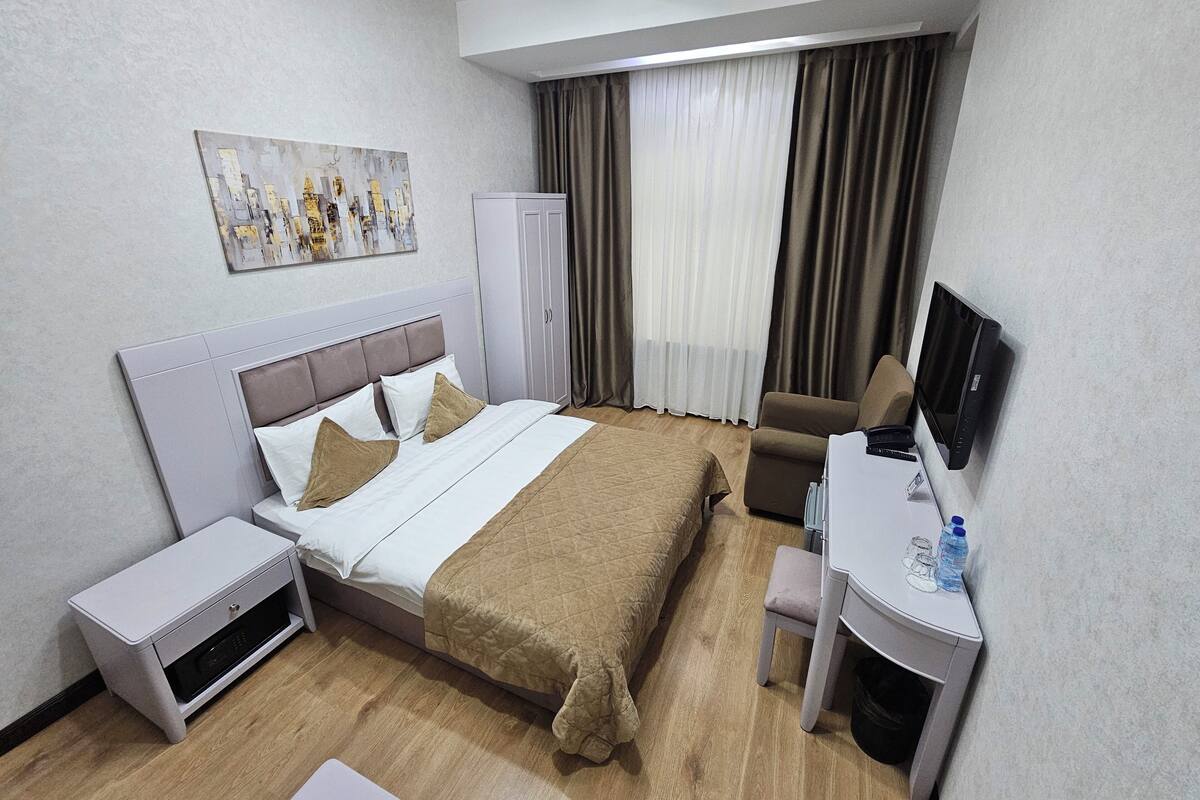 A hotel room with a bed, a desk with a computer, a TV, a wardrobe, and a painting on the wall.