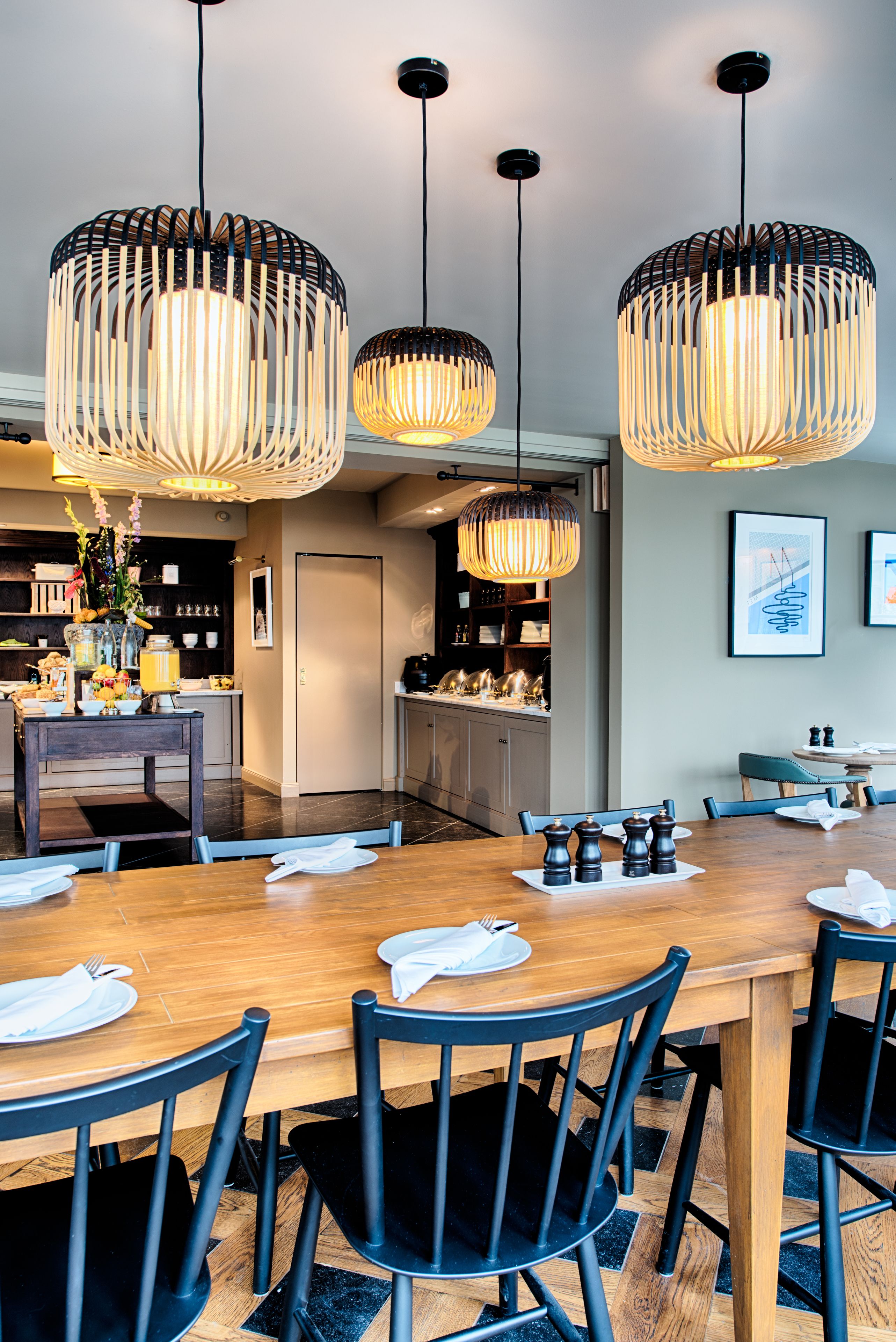 A dining area with a wooden table set for six, black chairs, and three hanging pendant lights.