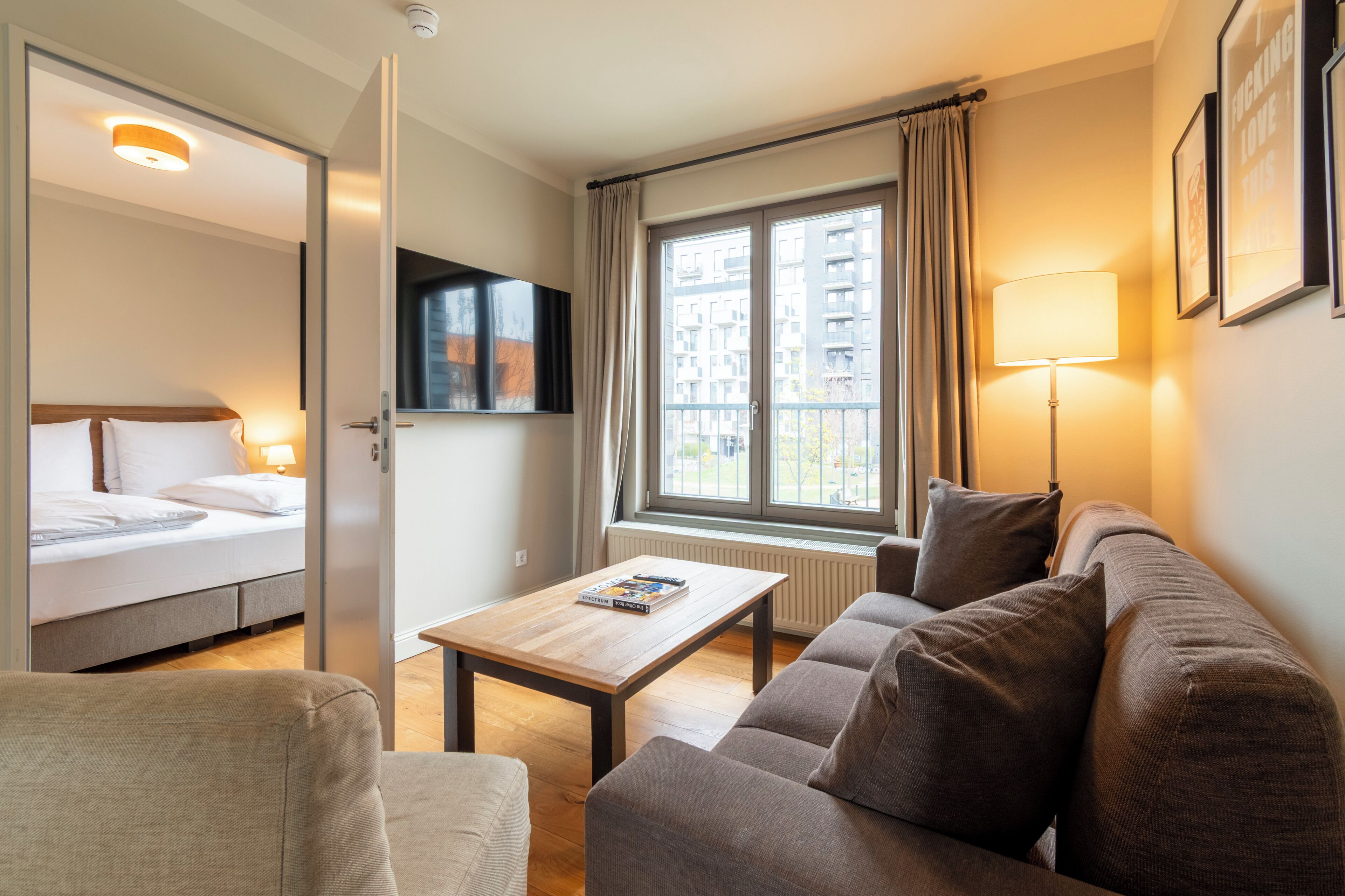 Ein Hotelzimmer mit Bett, Sofa, Tisch, Fernseher und einem Fenster mit Vorhängen.