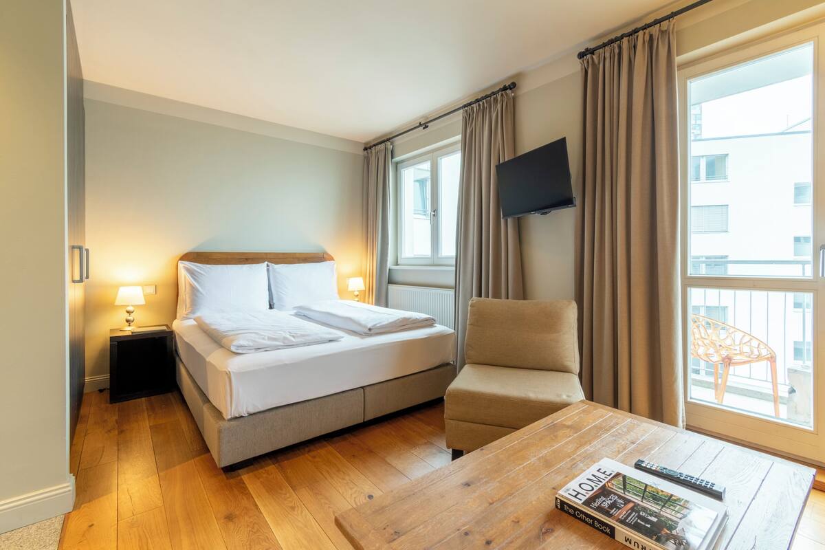 A hotel room with a bed, a chair, a coffee table, a TV, and a window with curtains.