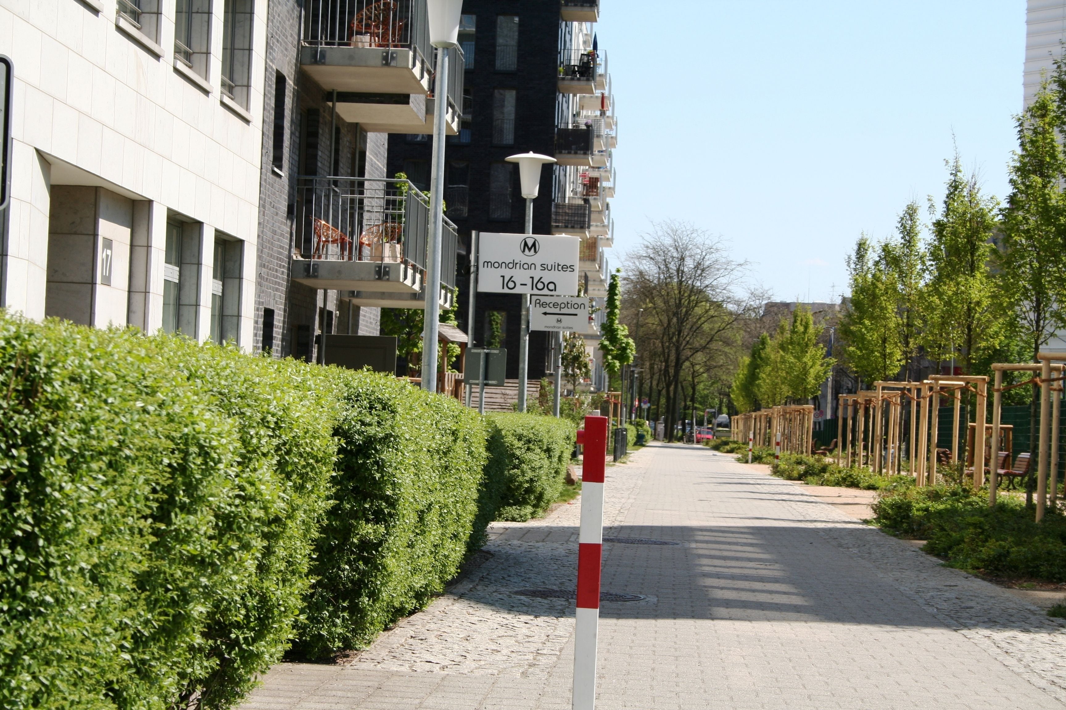A pathway lined with hedges and a building with balconies. There are signs indicating 'Mondrian Suites 16-16a' and 'Reception'.