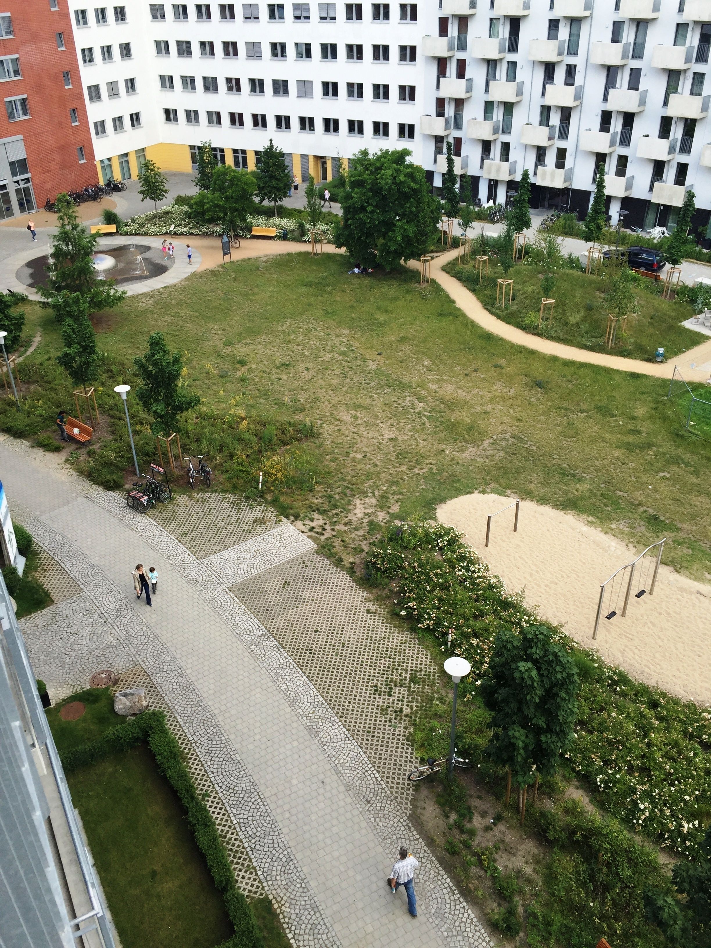 An aerial view of a residential area with a paved walkway, green spaces, and a multi-story building with balconies.