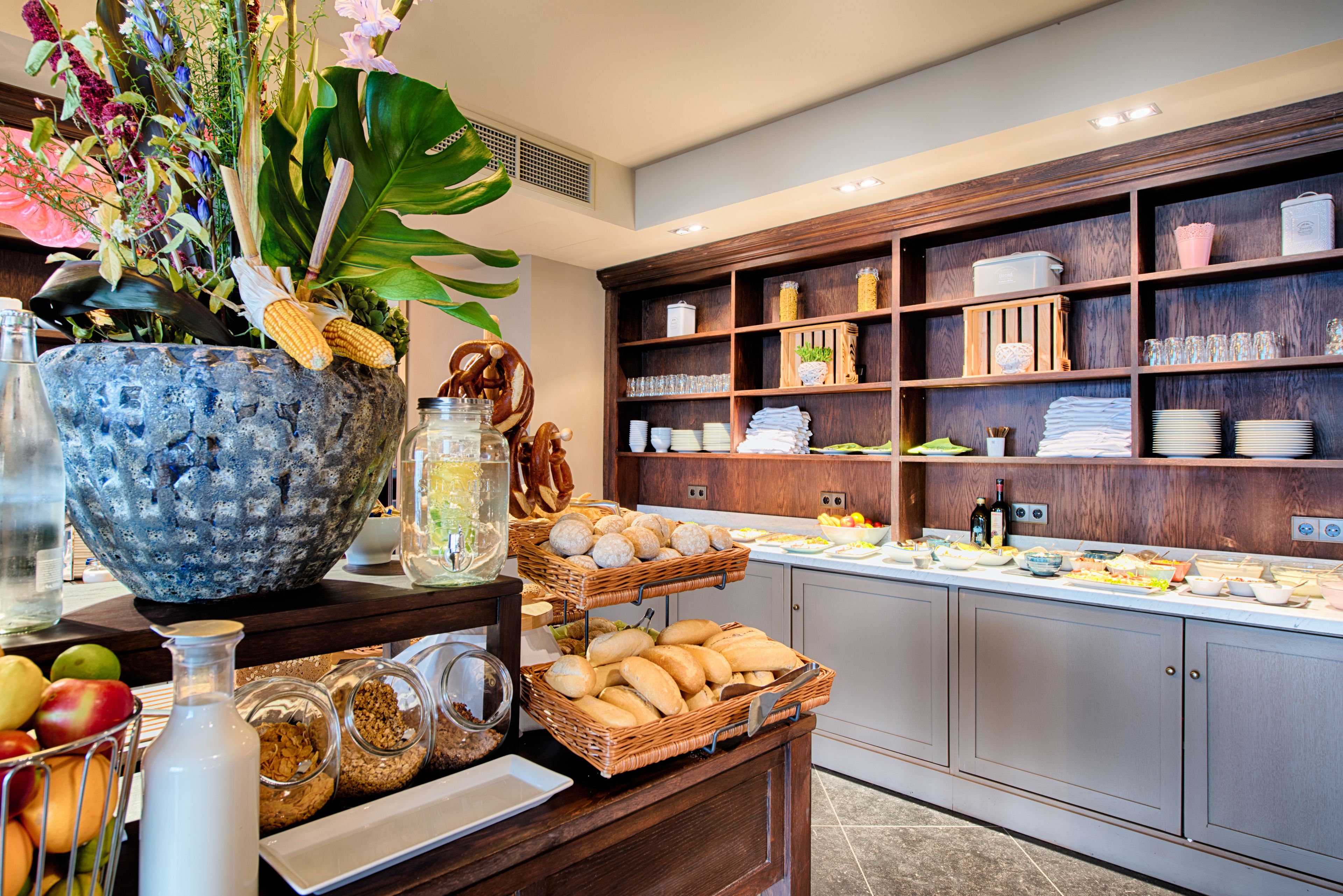 A buffet area with various food items, a decorative plant, and neatly arranged shelves with glassware and dishes.