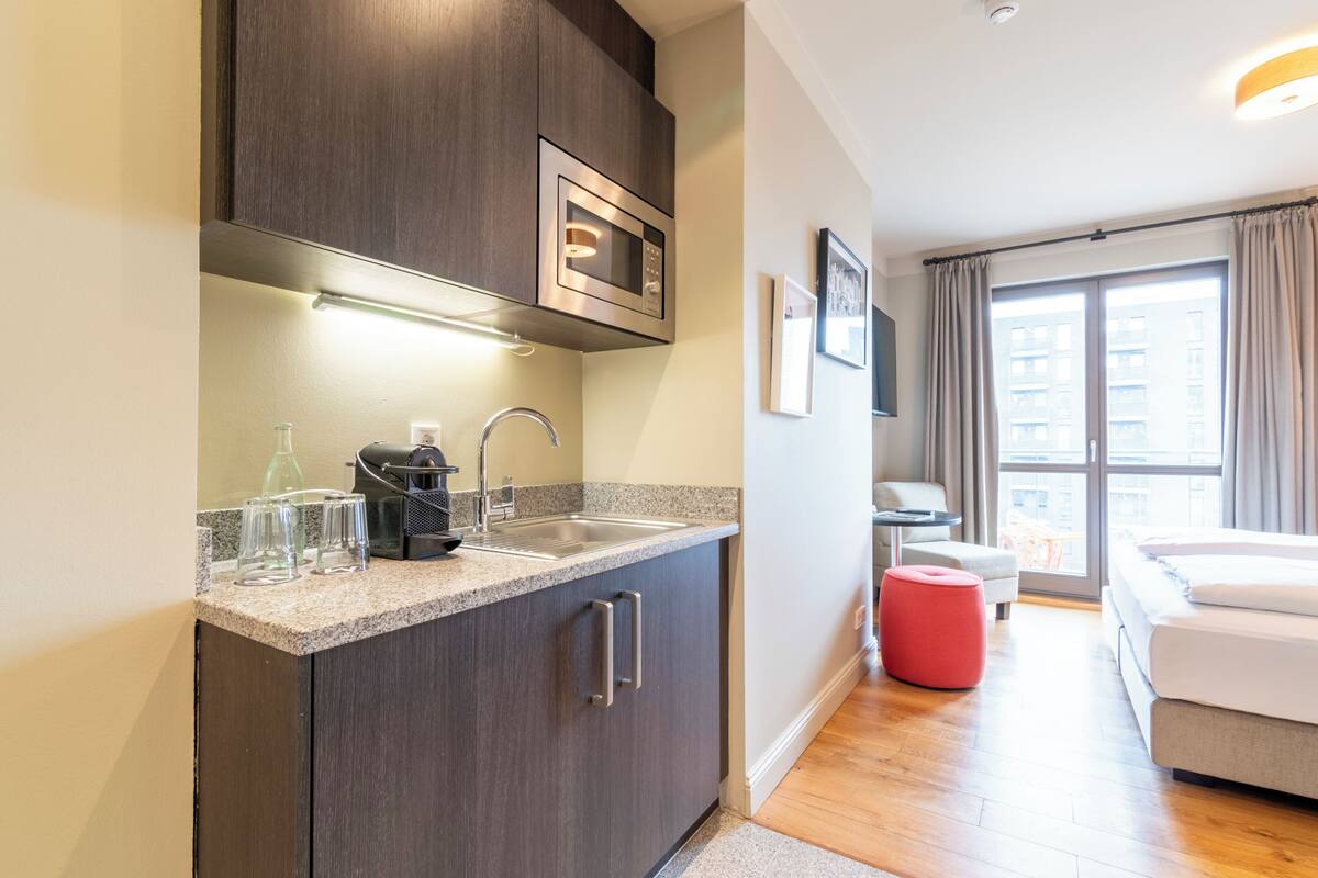 A modern kitchen with a built-in microwave, a sink, and a countertop with glasses and a coffee maker.