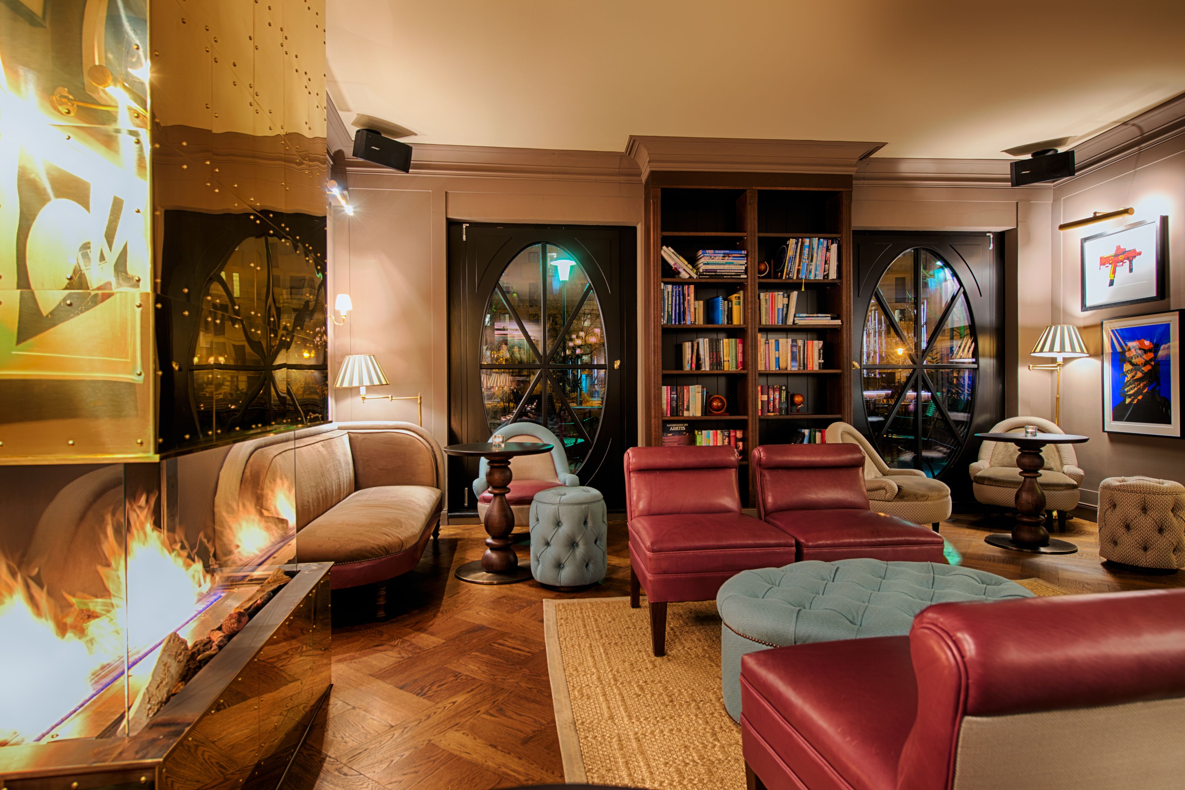 A cozy living room with a fireplace, leather sofas, a bookshelf, and a large window with a view.