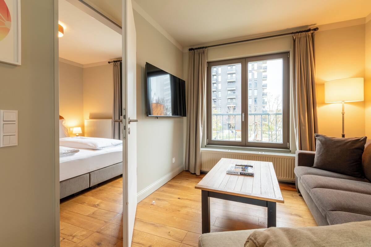 A hotel room with a bed, a TV, a window with curtains, a sofa, and a coffee table.