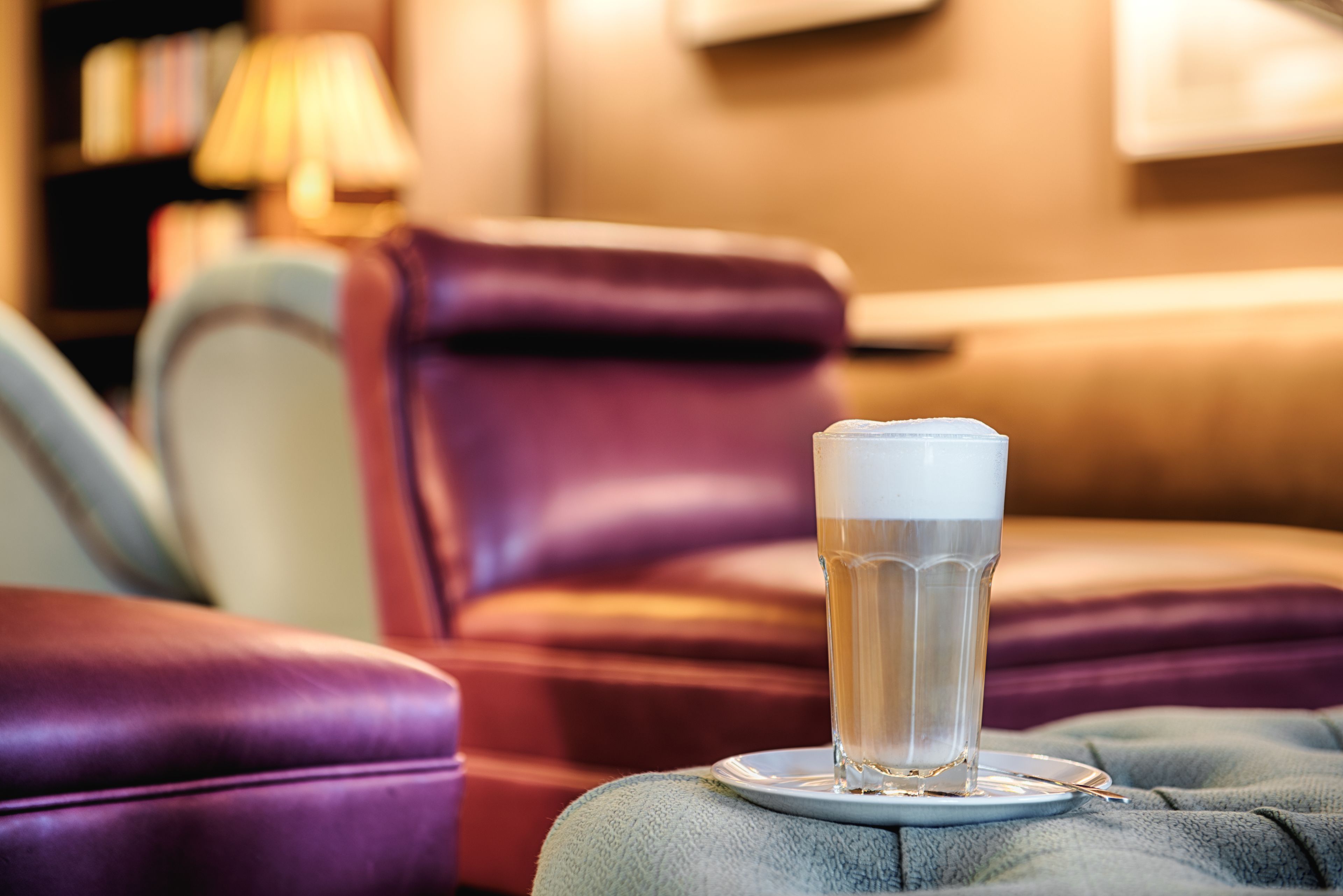 A glass of beer on a coaster on a cushioned ottoman in a room with leather furniture.