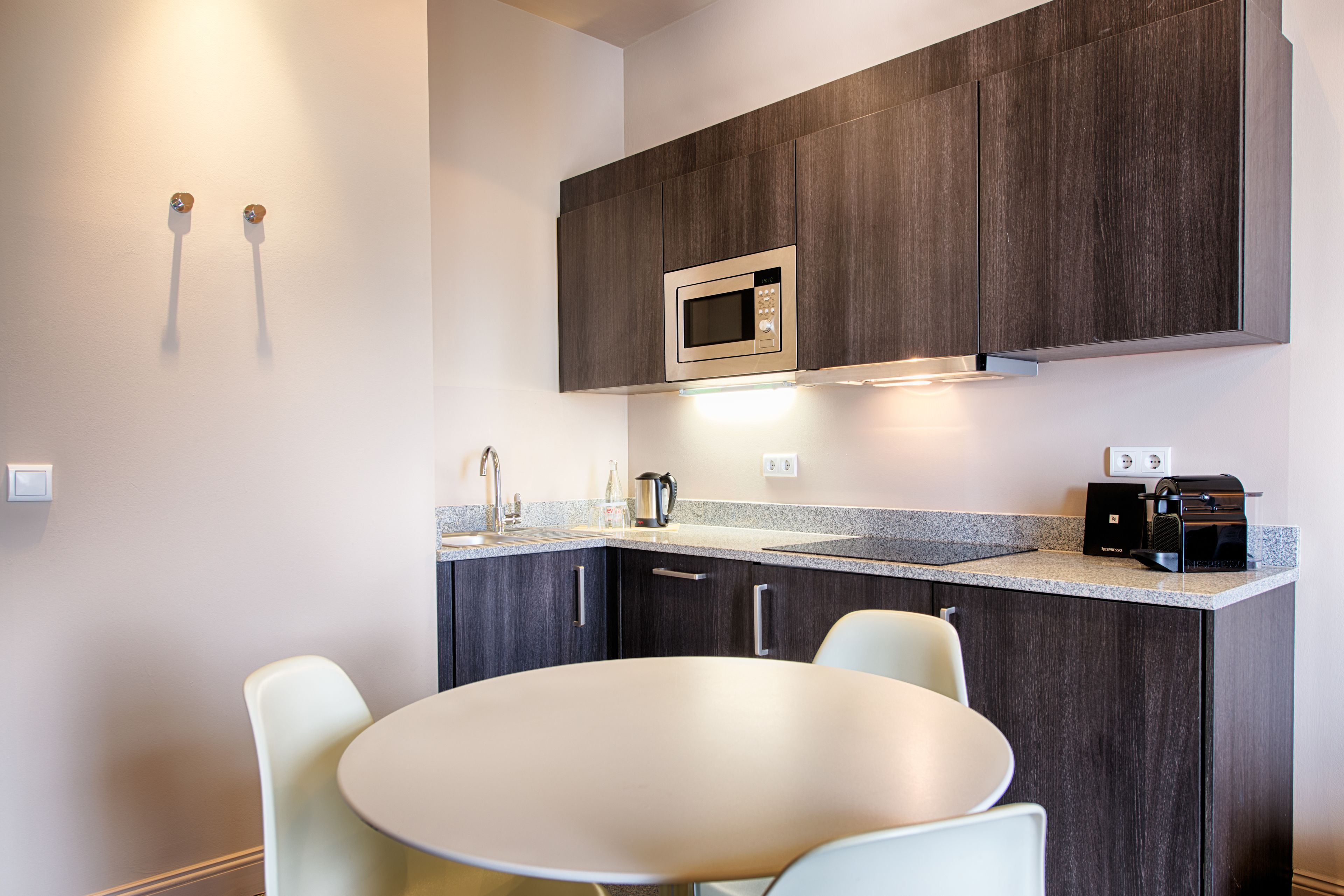 Een moderne keuken met donkerhouten kasten, een roestvrijstalen magnetron, een koffiezetapparaat en een ronde tafel met twee stoelen.