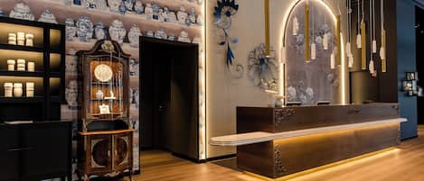 A reception area with a wooden reception desk, a wall of blue and white porcelain vases, and a decorative wall piece.