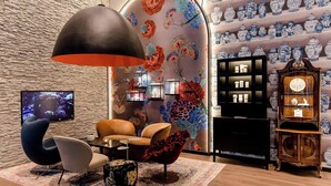 A modern interior with a stone wall, a large hanging light fixture, a television, and a wall of blue and white vases. - Motel One Dresden Am Zwinger (Dresden)