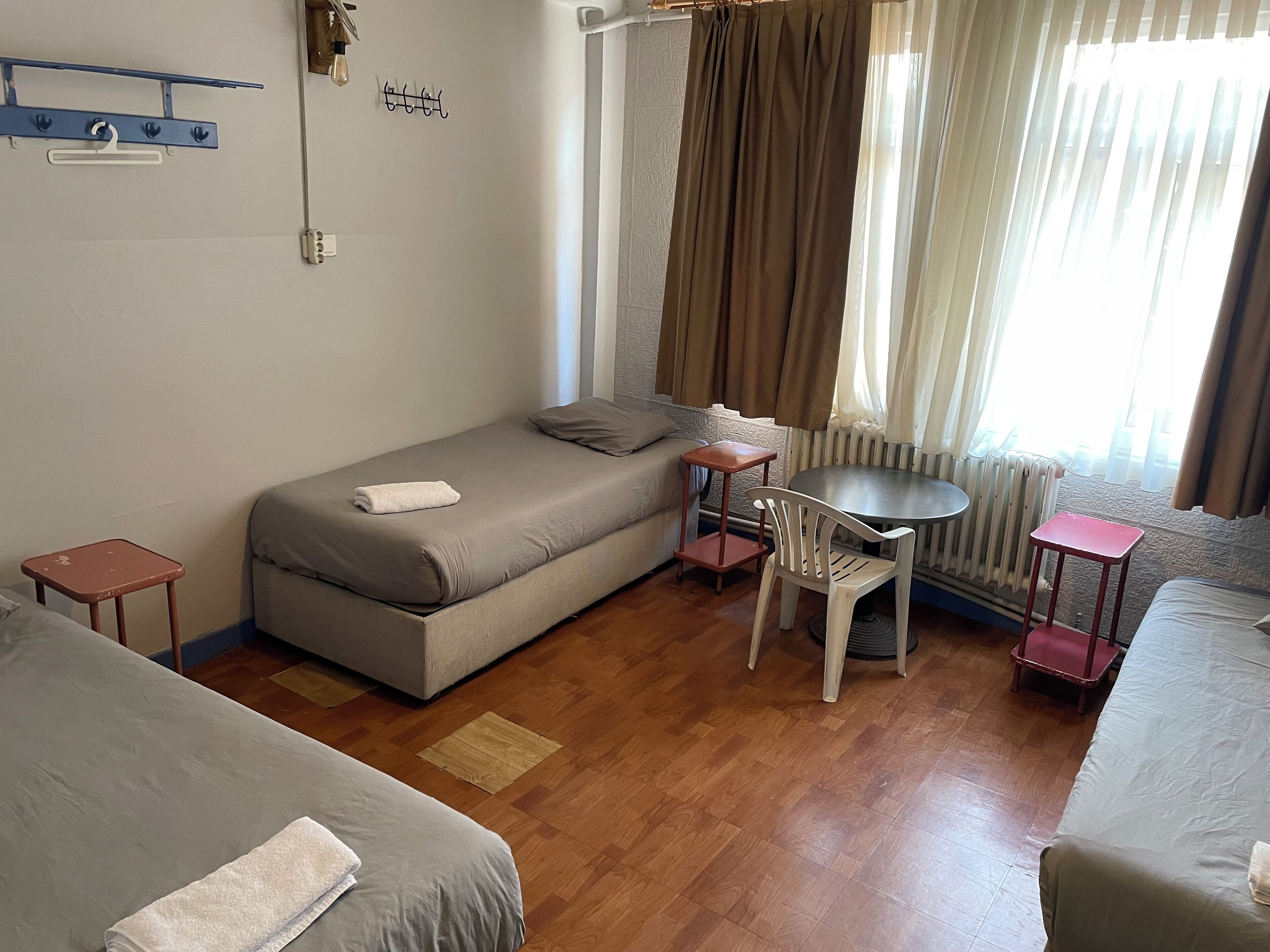 A compact hotel room with a single bed, a small table, a chair, and a radiator.