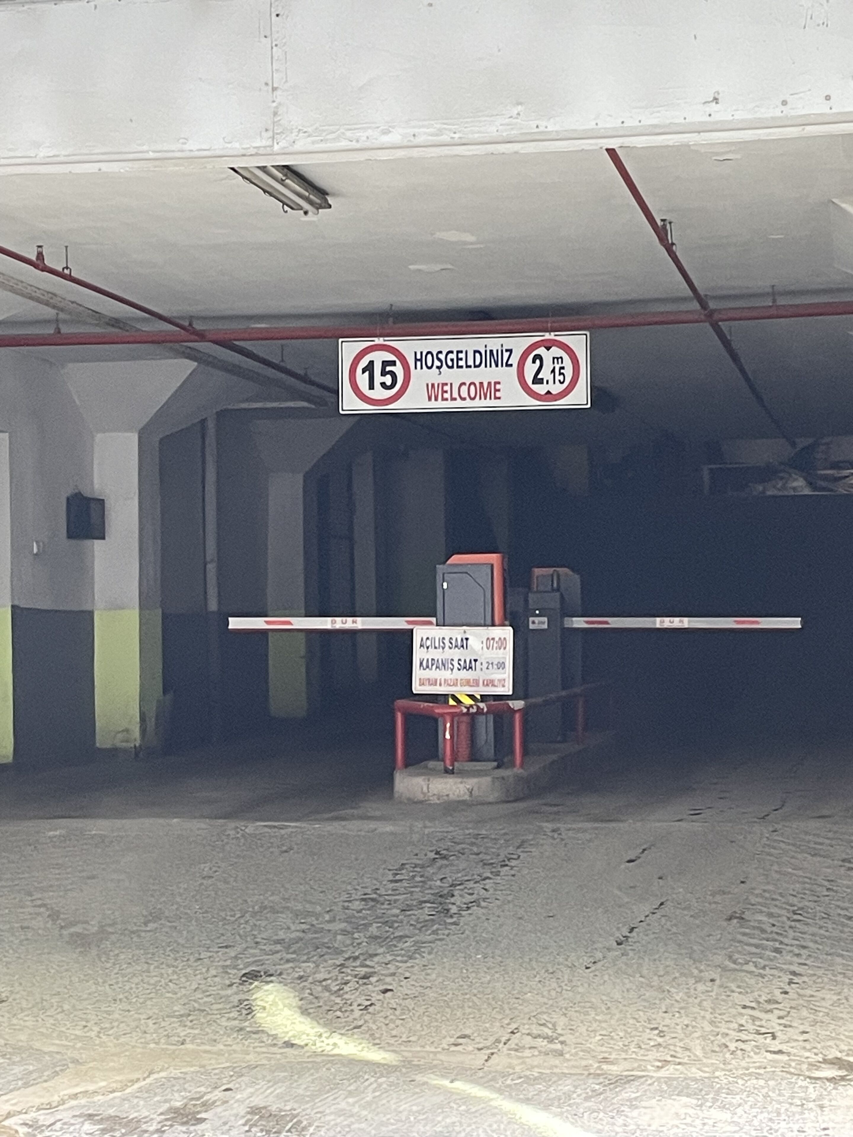 A parking garage entrance with a welcome sign, a speed limit sign, and a barrier gate.