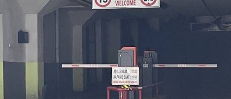 A parking garage entrance with a welcome sign, a speed limit sign, and a barrier gate.