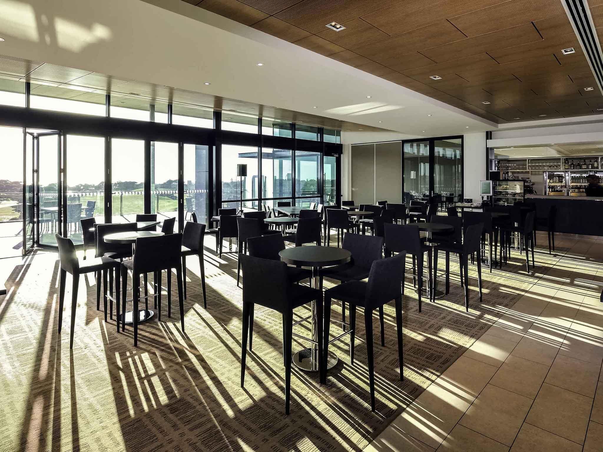 A modern dining area with large windows, tables, and chairs, and a bar area.