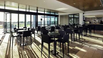 A modern dining area with large windows, tables, and chairs, and a bar area.