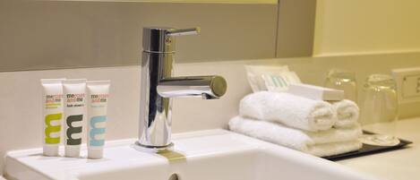 A bathroom sink with a chrome faucet, three tubes of shampoo, and neatly folded towels.