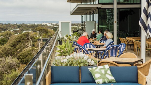 Una terraza con mesas al aire libre, vistas del paisaje y un edificio con grandes ventanales.