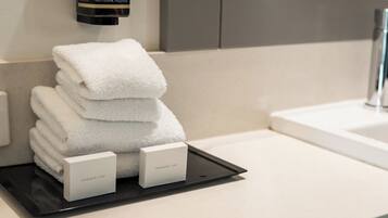 A stack of white towels on a tray with two labeled boxes, a black bottle, and a modern bathroom sink.