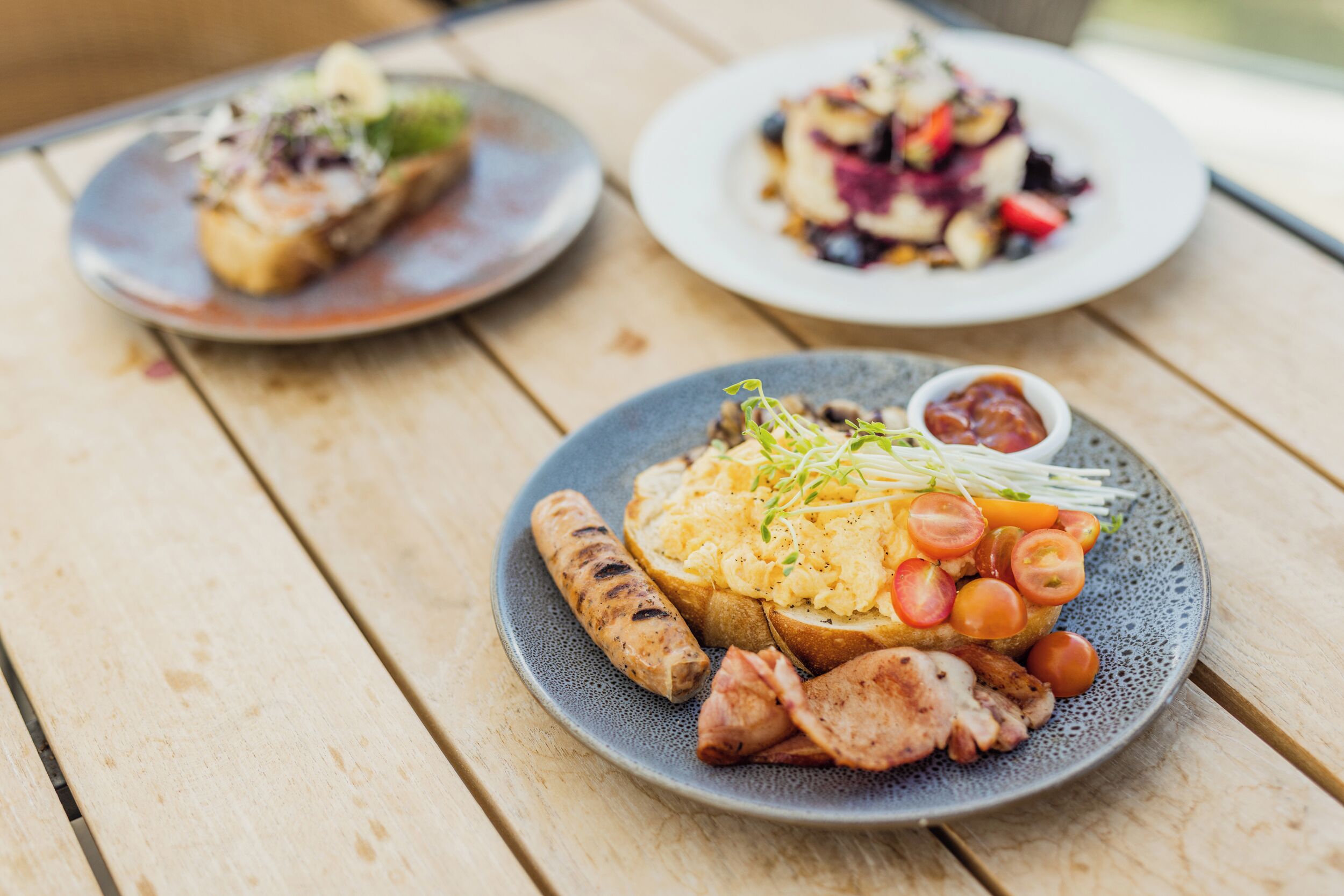 A wooden table with three plates of food.