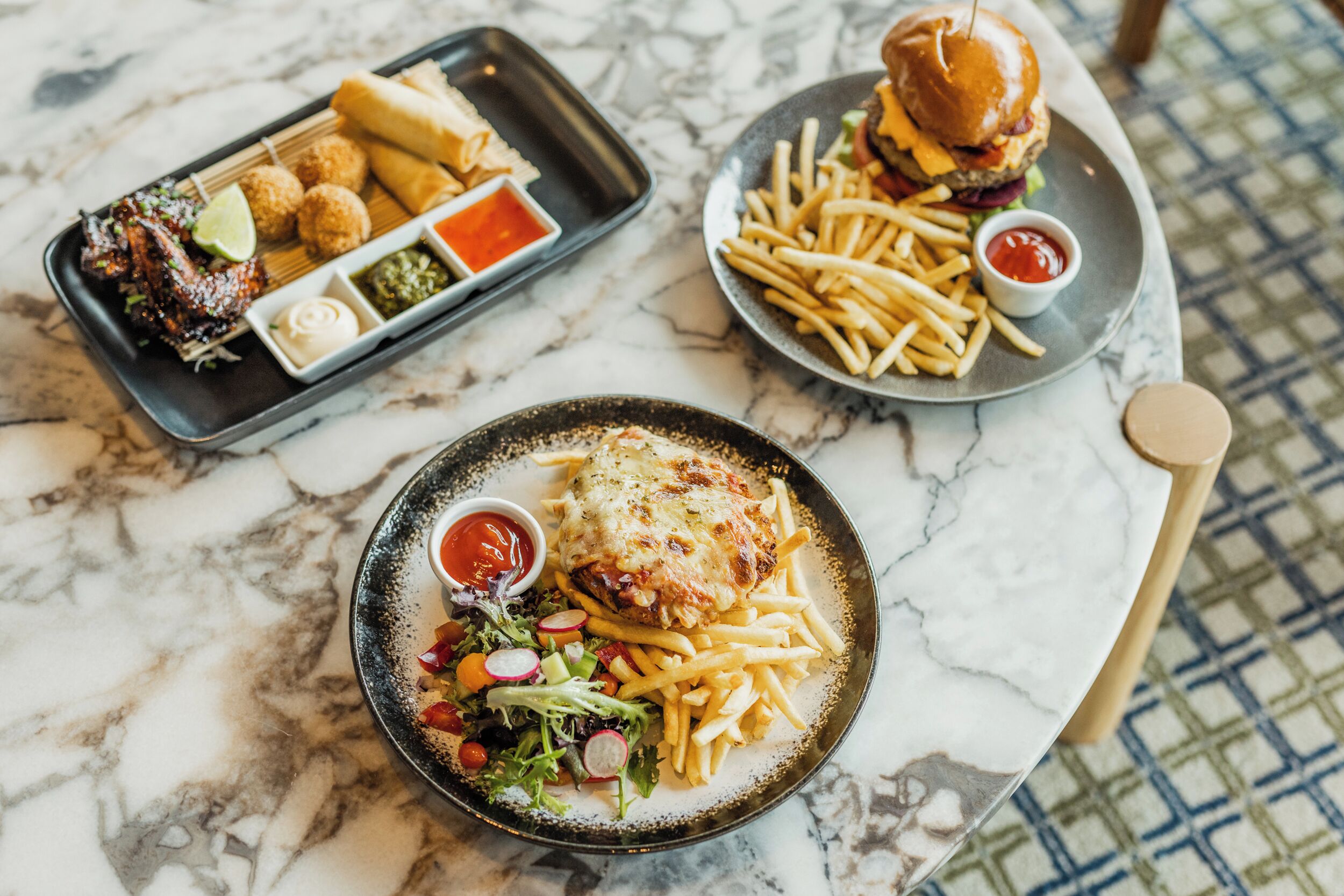 A dining table with three plates of food, including a burger, fries, and a salad.