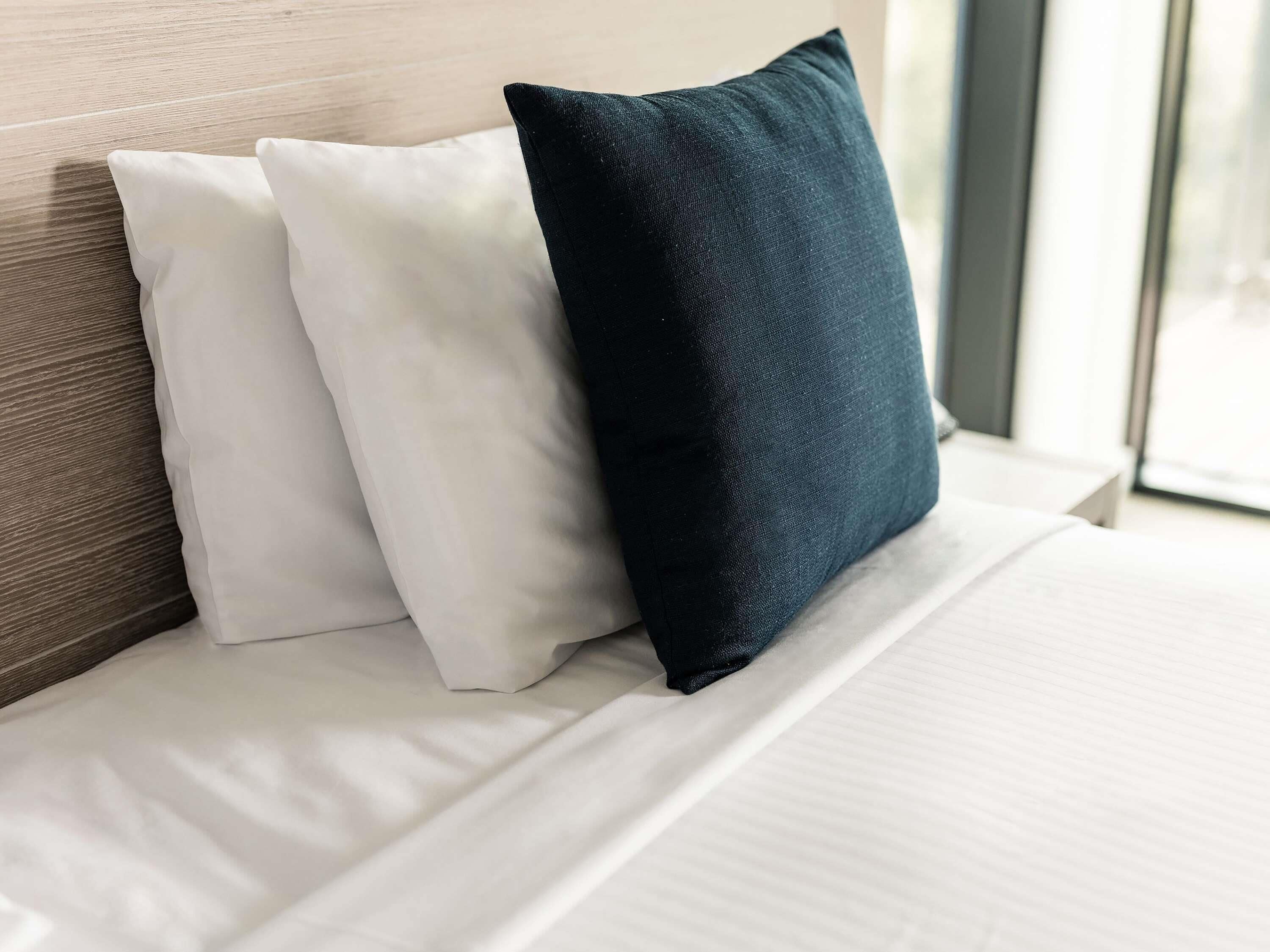 A bed with two pillows, one white and one dark blue, against a wooden headboard.