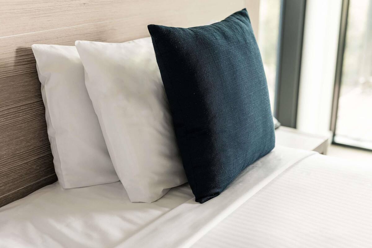 A bed with two pillows, one white and one dark blue, against a wooden headboard.